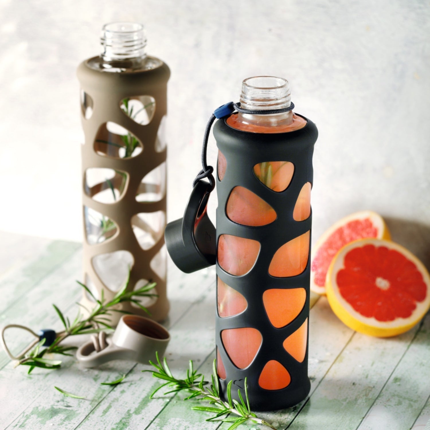 Zwei Glasflaschen mit Silikonhülle und Grapefruit-Drink auf grünem Holztisch
