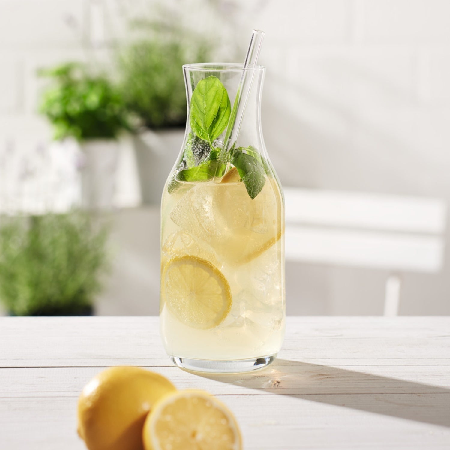 Karaffe mit Zitronenlimonade, Eis und Basilikum auf weißem Tisch
