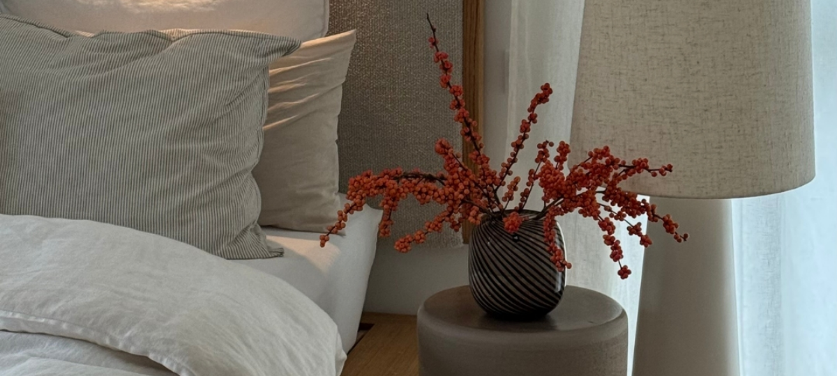 Wohnraumdetail mit grauem Sofa, Beistelltisch und Vase mit roten Beerenzweigen sowie dekorativen Vasen in Naturtönen.