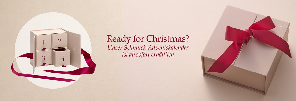Ready for Christmas? Unser Schmuck-Adventskalender ist ab sofort erhältlich. Elegante Geschenkbox mit roter Schleife und Adventskalender mit Bändern auf beigem Hintergrund