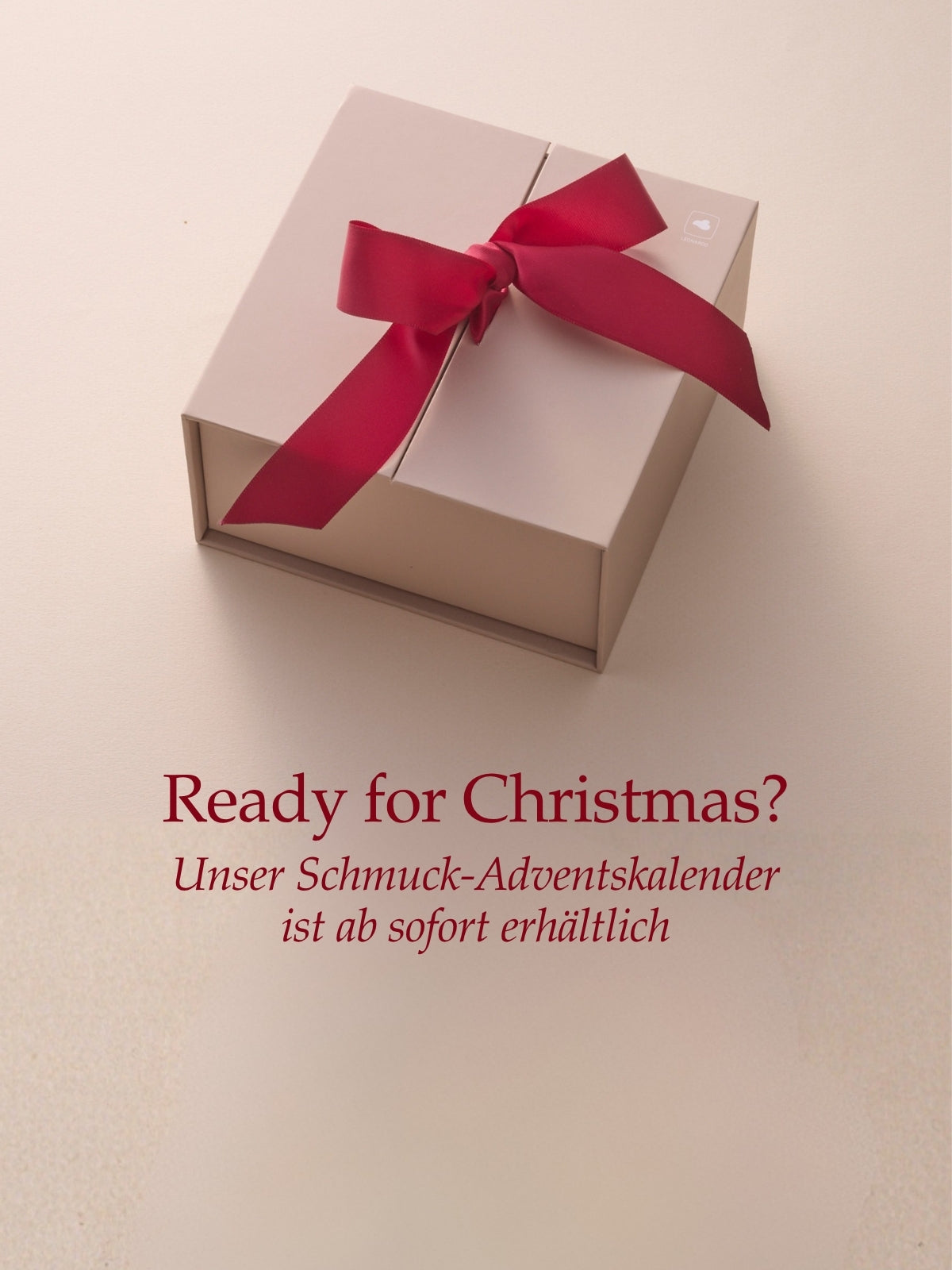 Ready for Christmas? Unser Schmuck-Adventskalender ist ab sofort erhältlich. Beige Geschenkbox mit roter Schleife auf hellem Untergrund