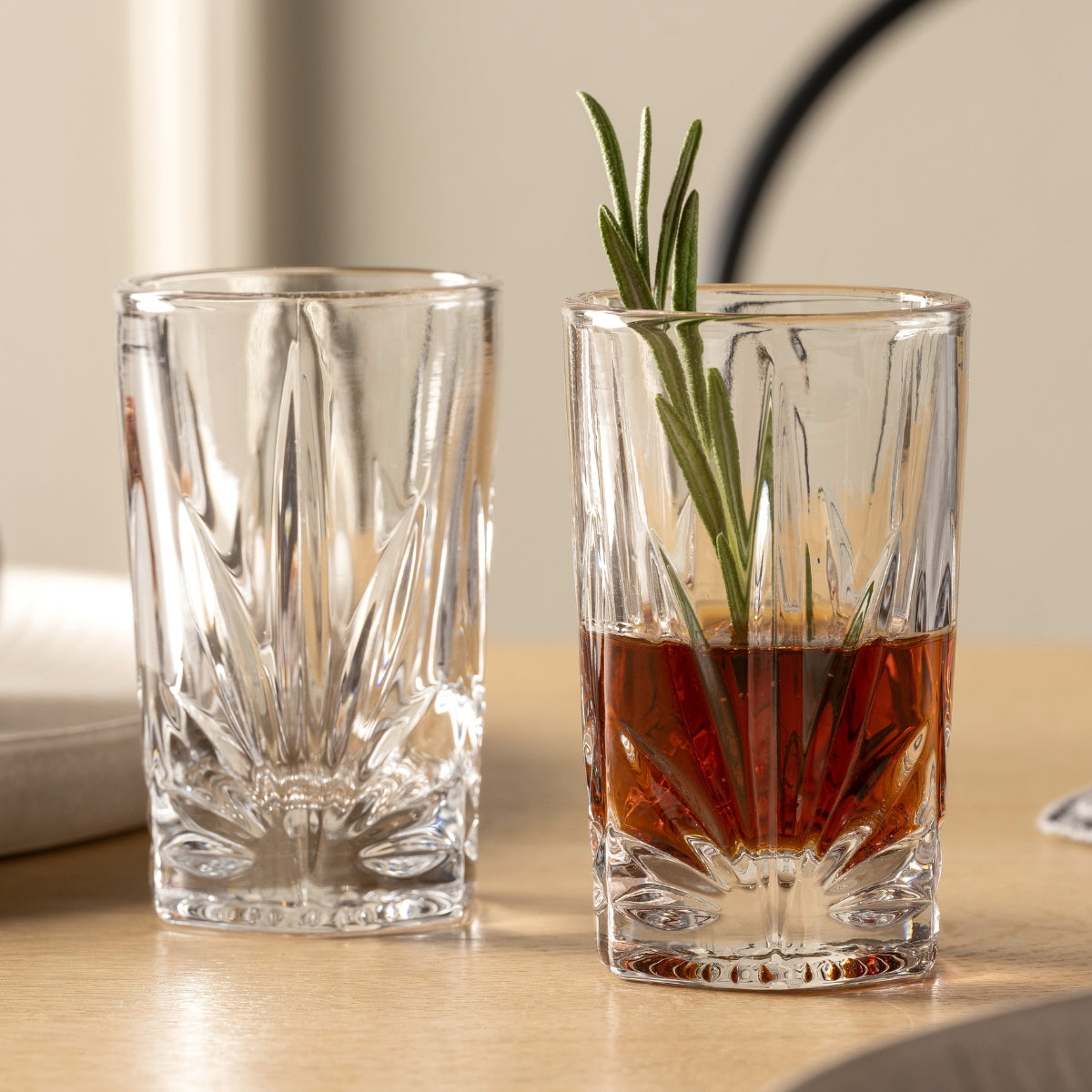 Zwei kleine Gläser, eines gefüllt mit einem dunklen Drink und dekoriert mit Rosmarin.