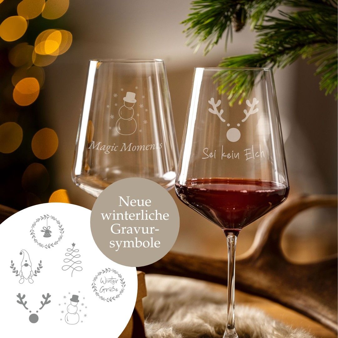 Zwei festlich gravierte Weingläser mit Weihnachtsmotiven vor stimmungsvoller Winterkulisse.