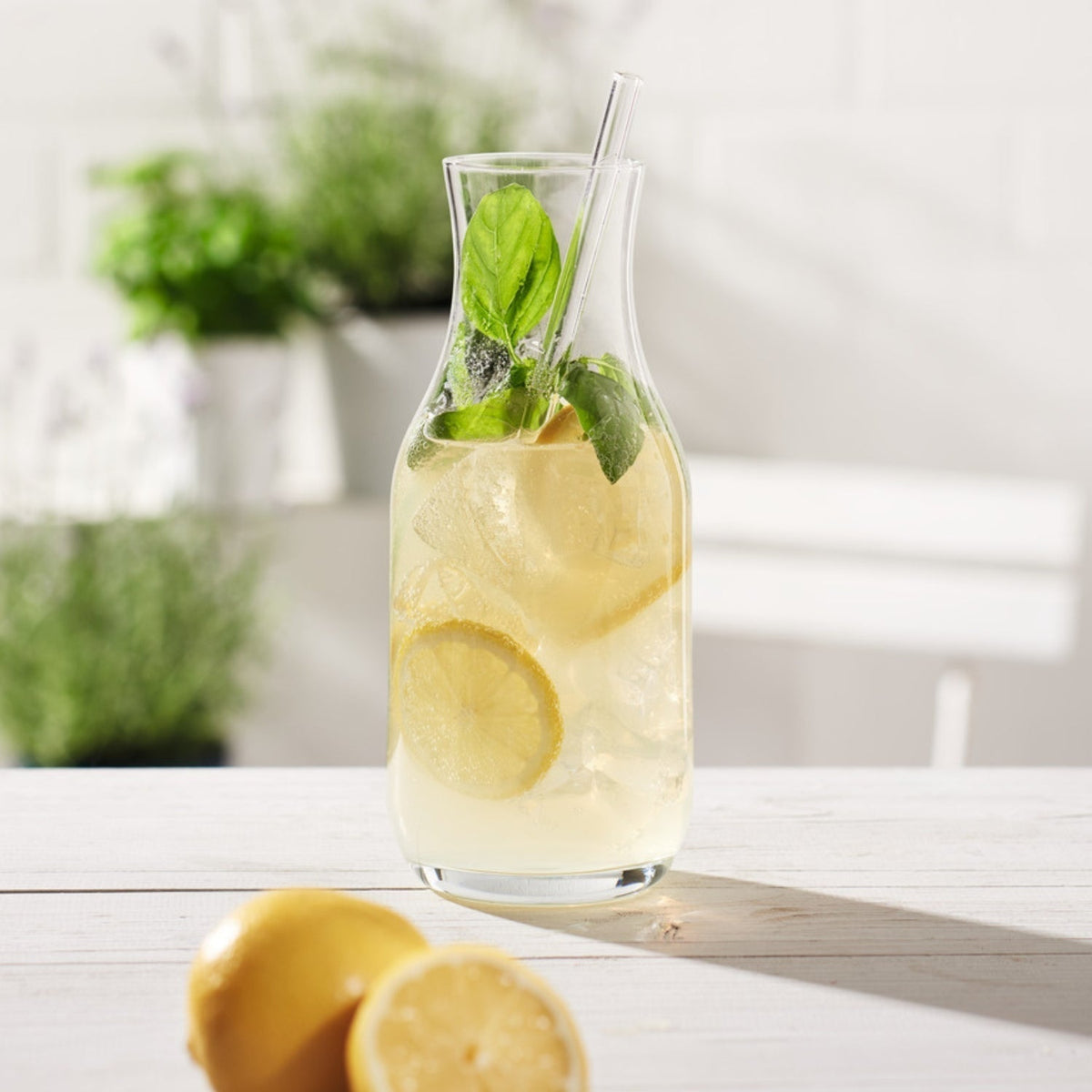 Karaffe mit Zitronenlimonade, Eis und Basilikum auf weißem Tisch