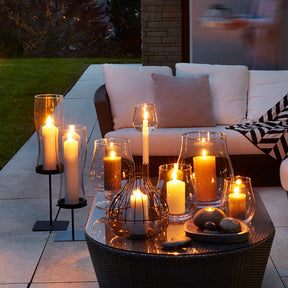Windlicht GIARDINO mit brennenden Kerzen auf Terrassentisch, Lounge-Möbel im Hintergrund