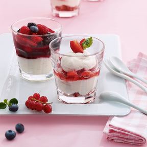 Zwei Gläser mit Beeren und Creme auf weißem Tablett, rosa Hintergrund