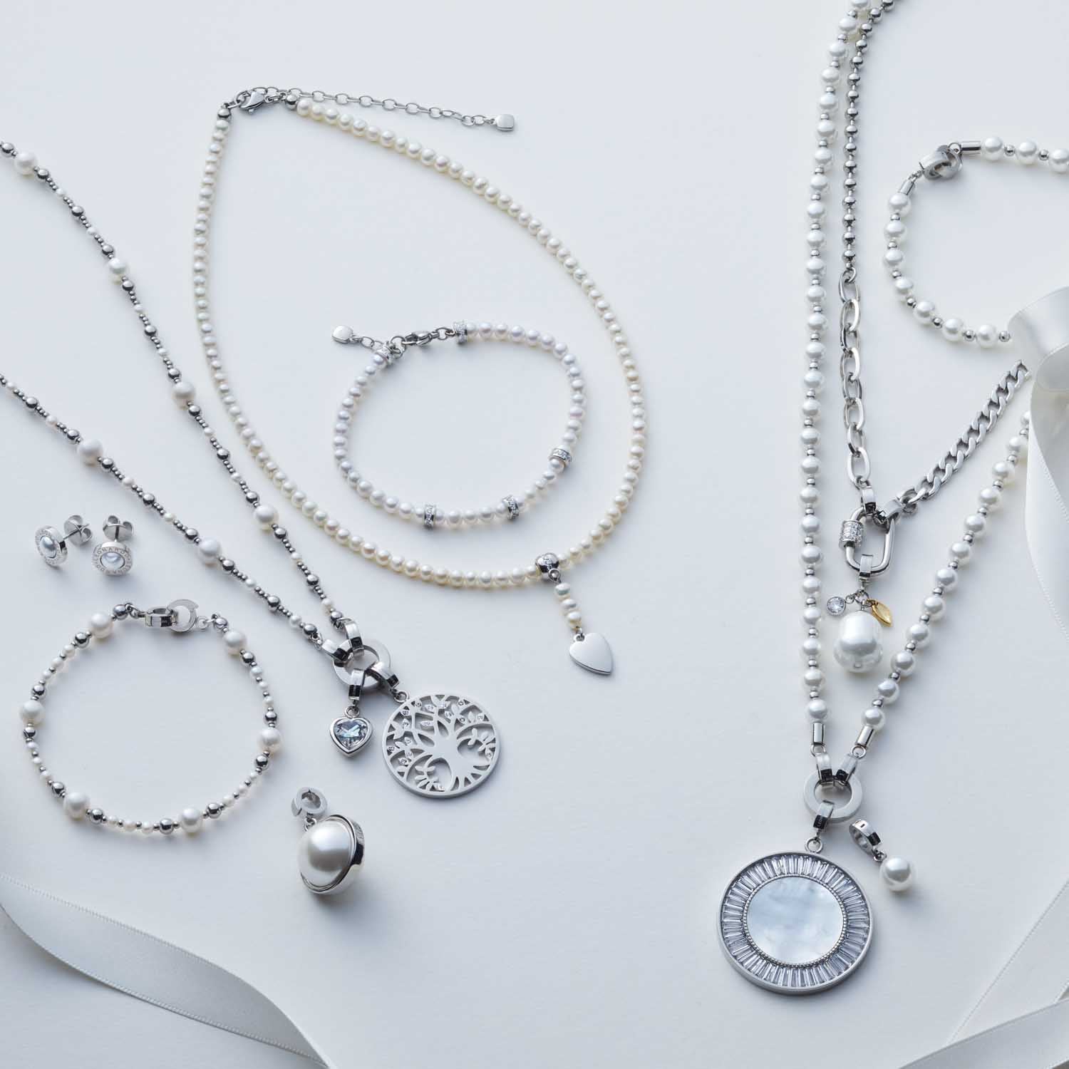 Schmuckkollektion mit Armbändern, Ketten und Anhängern in Weiß und Silber auf neutralem Hintergrund