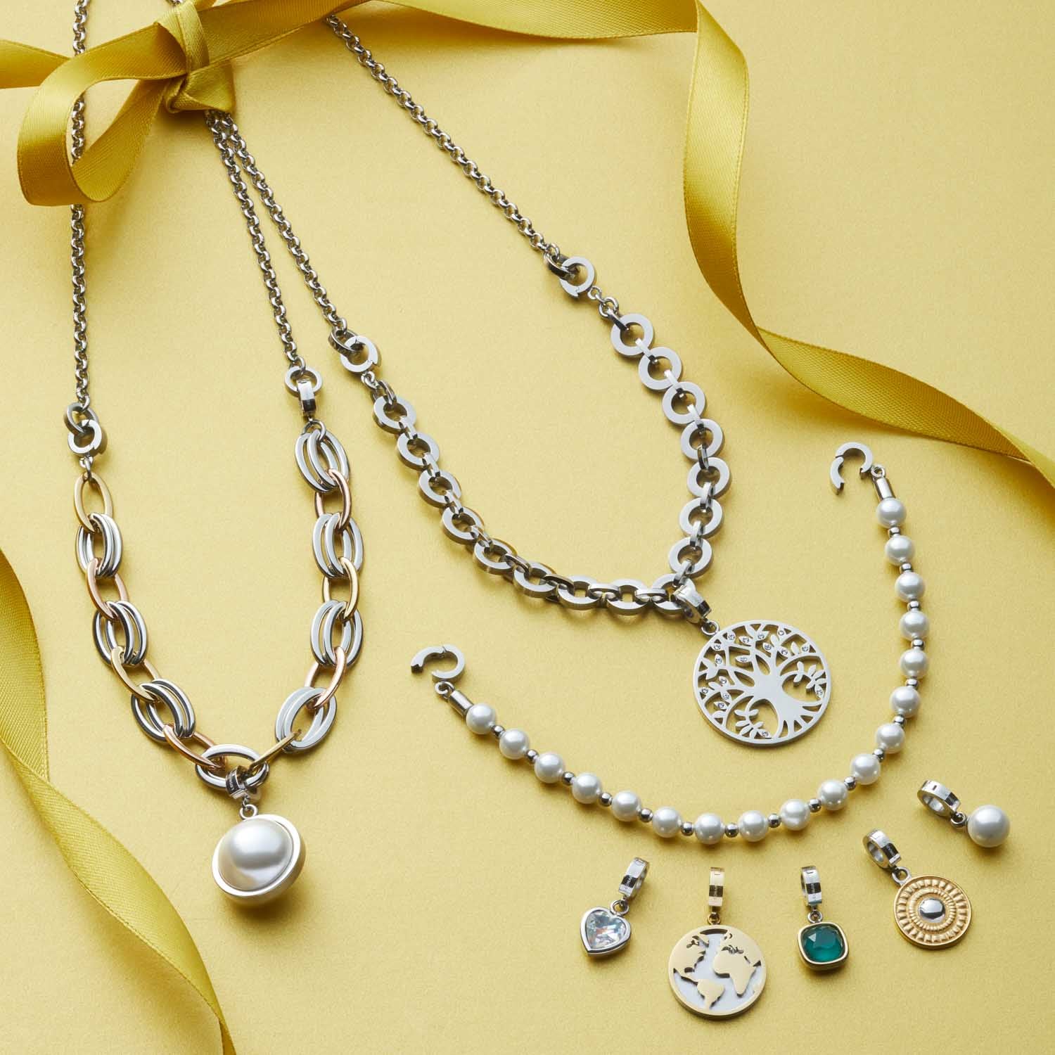 Schmuckkollektion mit Ketten, Armbändern und Charms auf gelbem Hintergrund mit Schleife