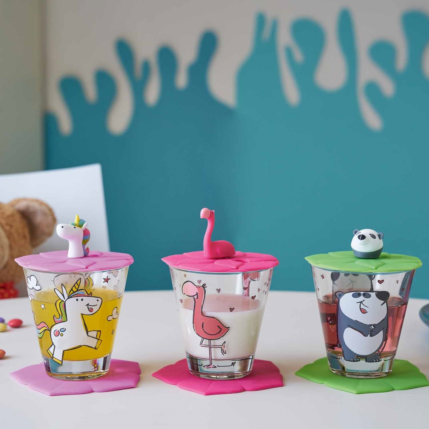 Drei Trinkgläser BAMBINI mit farbigen Silikon-Deckeln und Tiermotiven auf weißer Oberfläche
