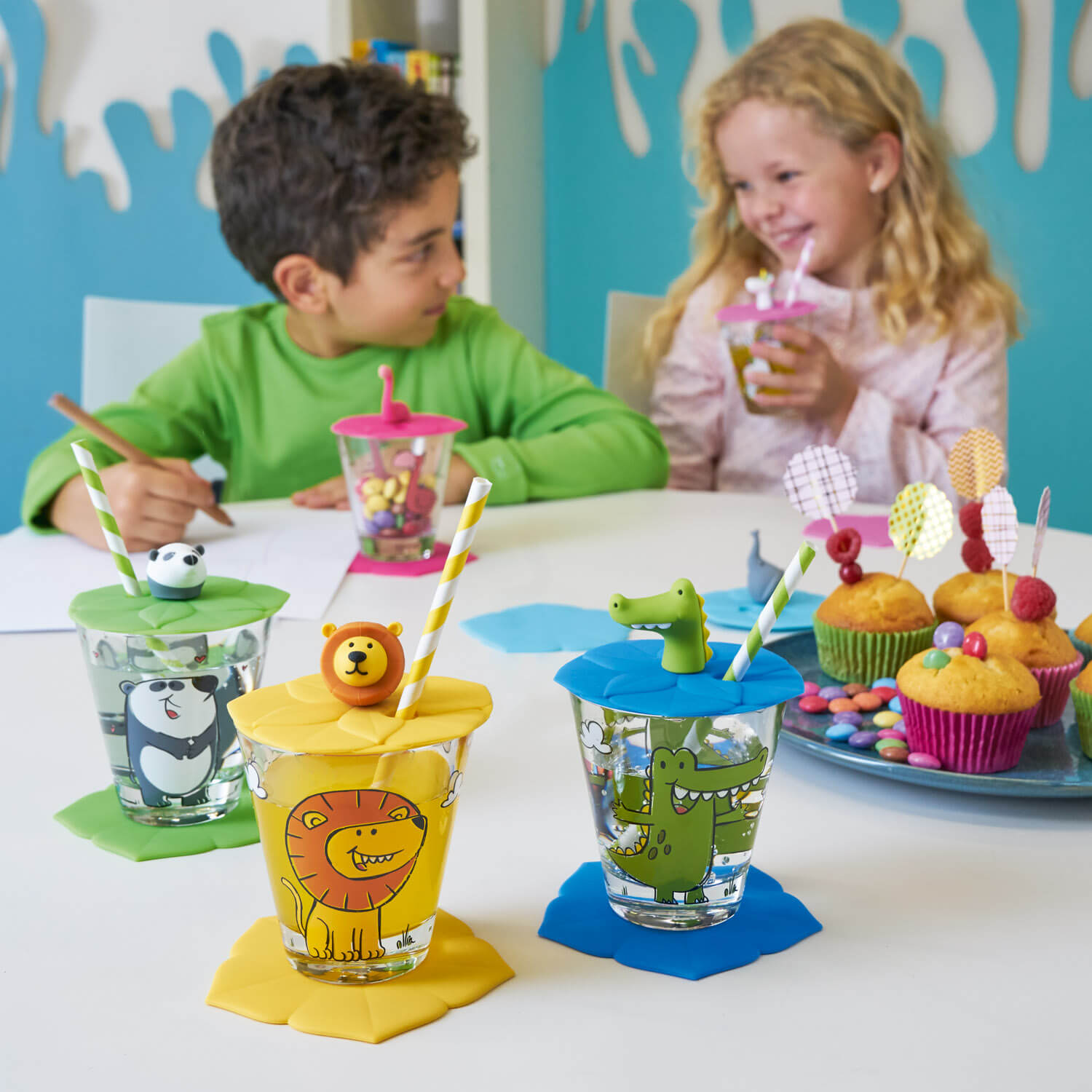Kinder beim Basteln an Tisch mit Silikon-Deckeln, gelber Löwen-Deckel prominent im Vordergrund