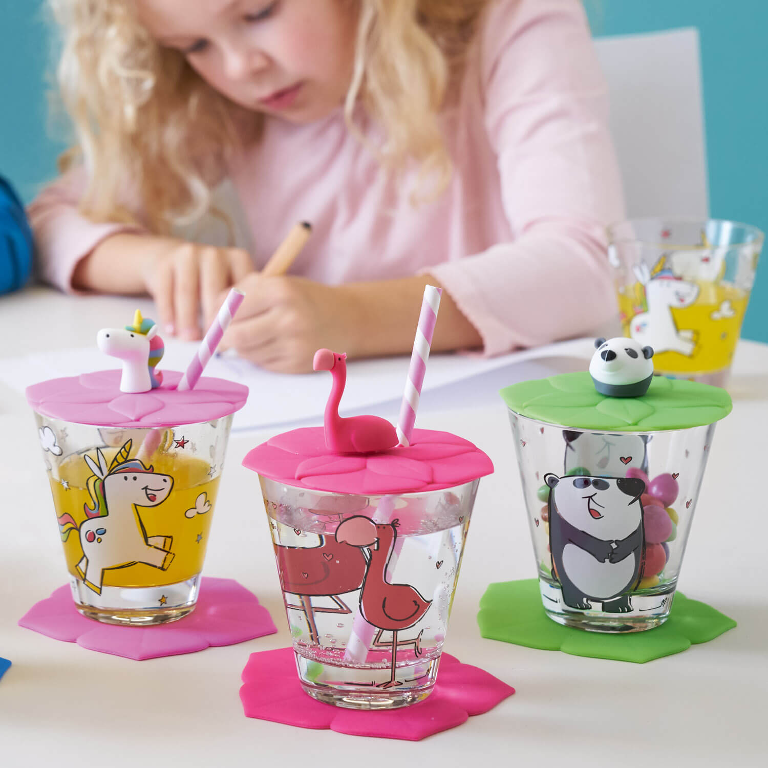 Drei bunte Silikondeckel auf Gläsern, Kind malt im Hintergrund