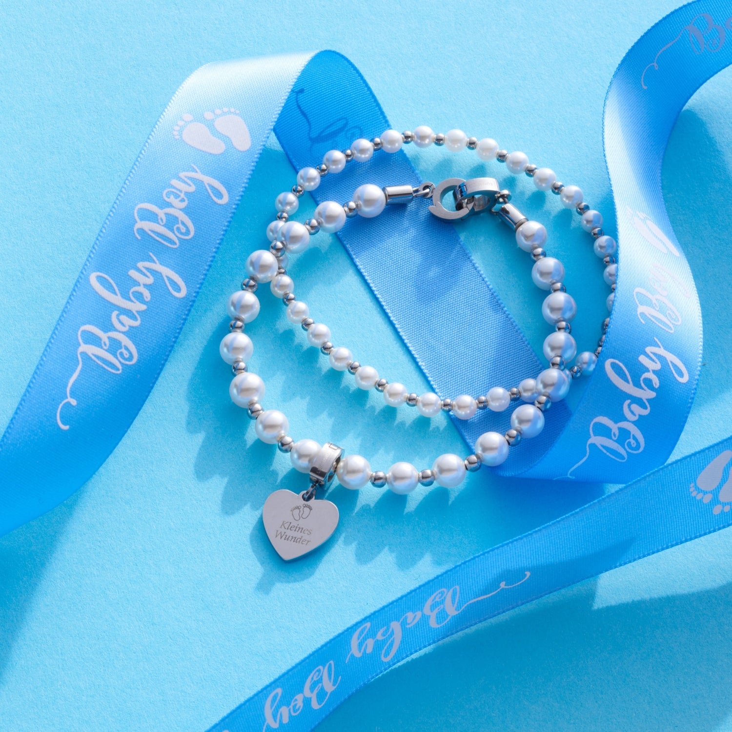 Anhänger JANA silber an Perlenarmband mit blauem Band auf hellblauem Untergrund