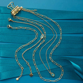 Mehrere goldene Ketten auf türkisblauem Hintergrund mit Binder-Clip