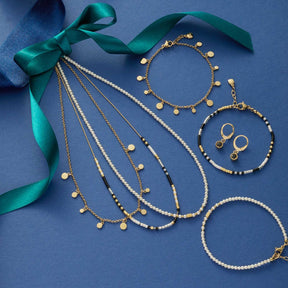 Halskette DORO mit Muscheln, Armbändern, Ohrringen und grünem Seidenband auf blauem Hintergrund