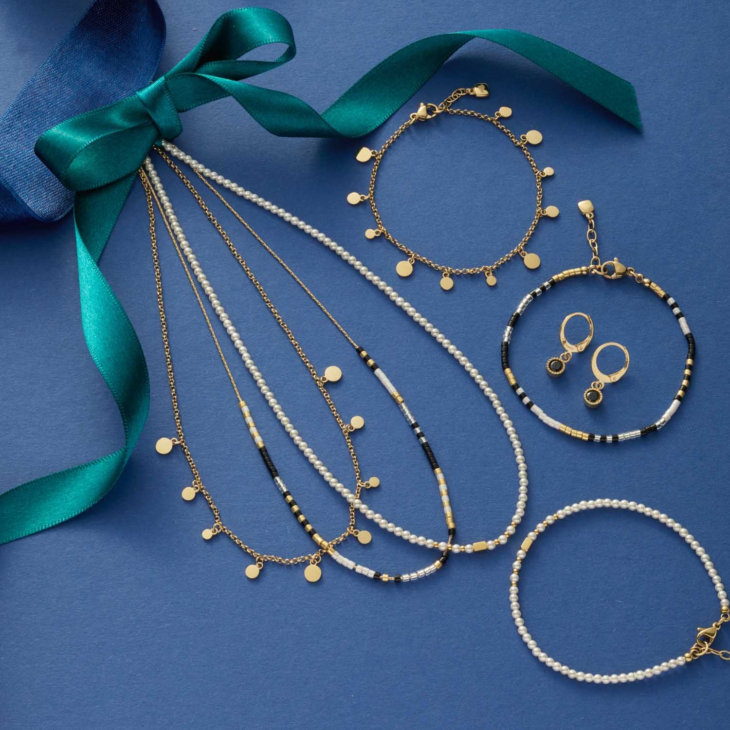 Schmuckkollektion mit Armbändern, Ohrringen und grünem Band auf blauem Hintergrund