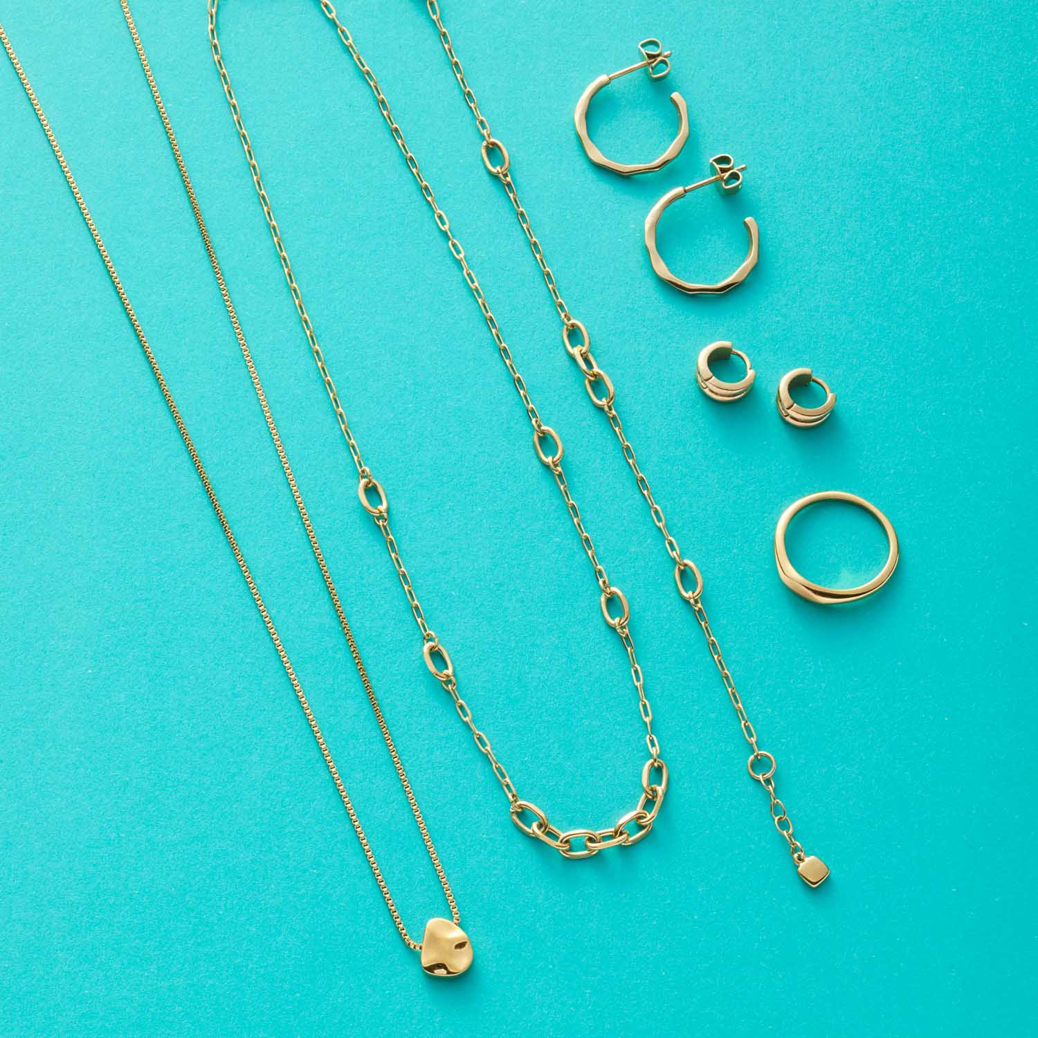 Schmuckkollektion mit goldenen Ketten, Ringen und Ohrringen auf türkisem Hintergrund