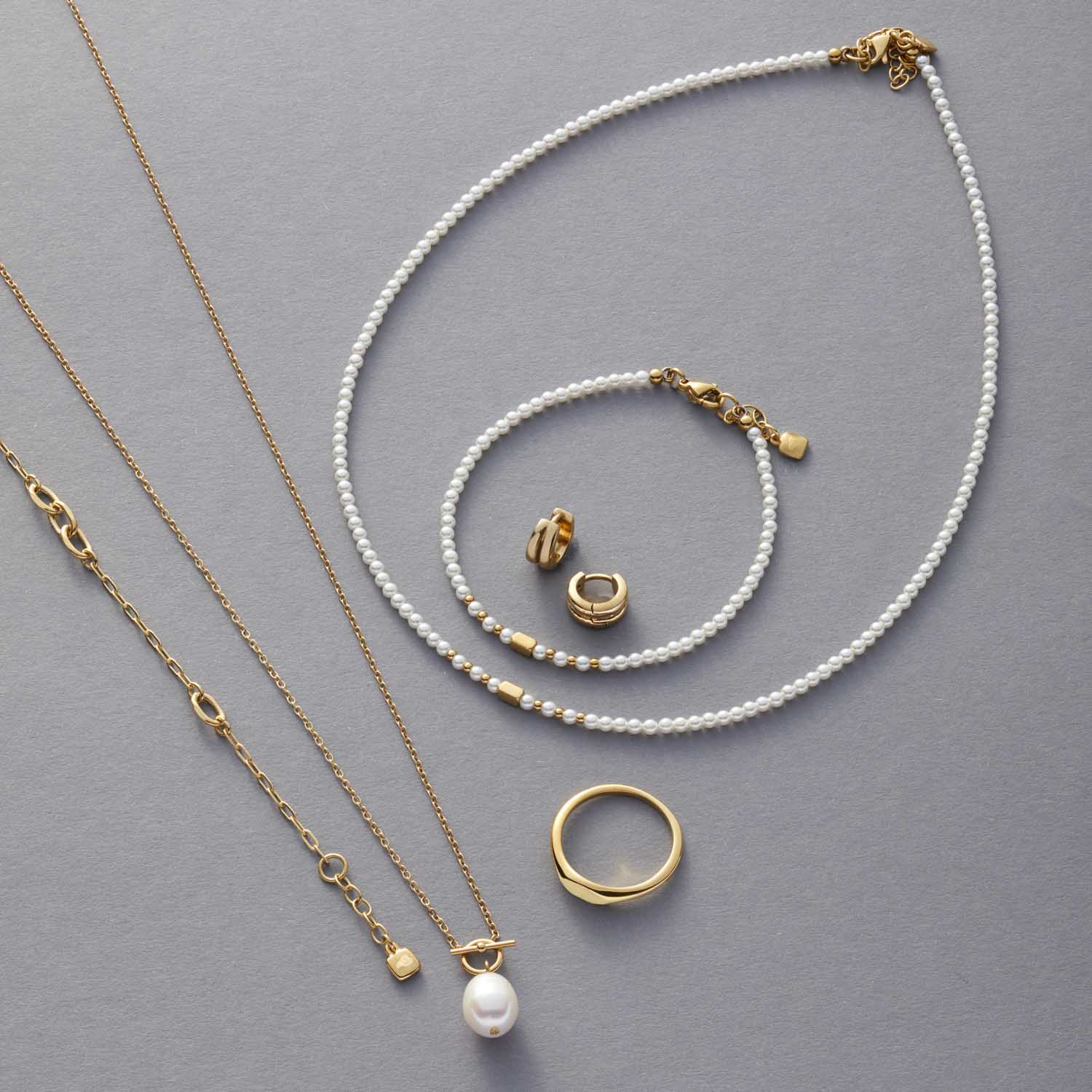 Schmuckkollektion mit goldfarbenen Ringen, Perlenarmbändern und Halsketten auf grauem Hintergrund