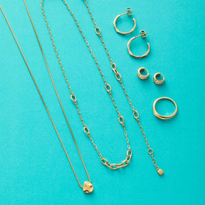 Goldene Schmuckkollektion mit Halsketten, Ringen und Ohrringen auf türkisem Hintergrund