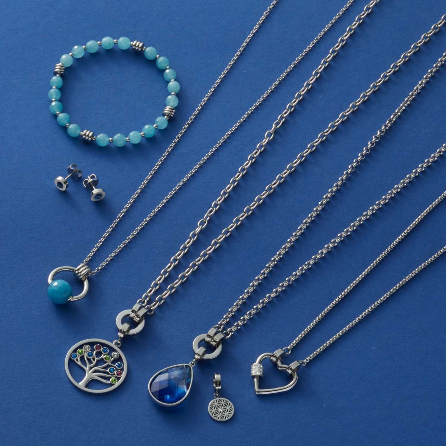Silberne Halsketten mit Anhängern, grünes Armband und Ohrstecker auf blauem Hintergrund