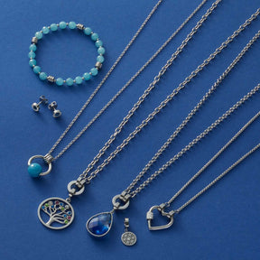 Silberne Halsketten mit Anhängern, grünes Armband und Ohrstecker auf blauem Hintergrund