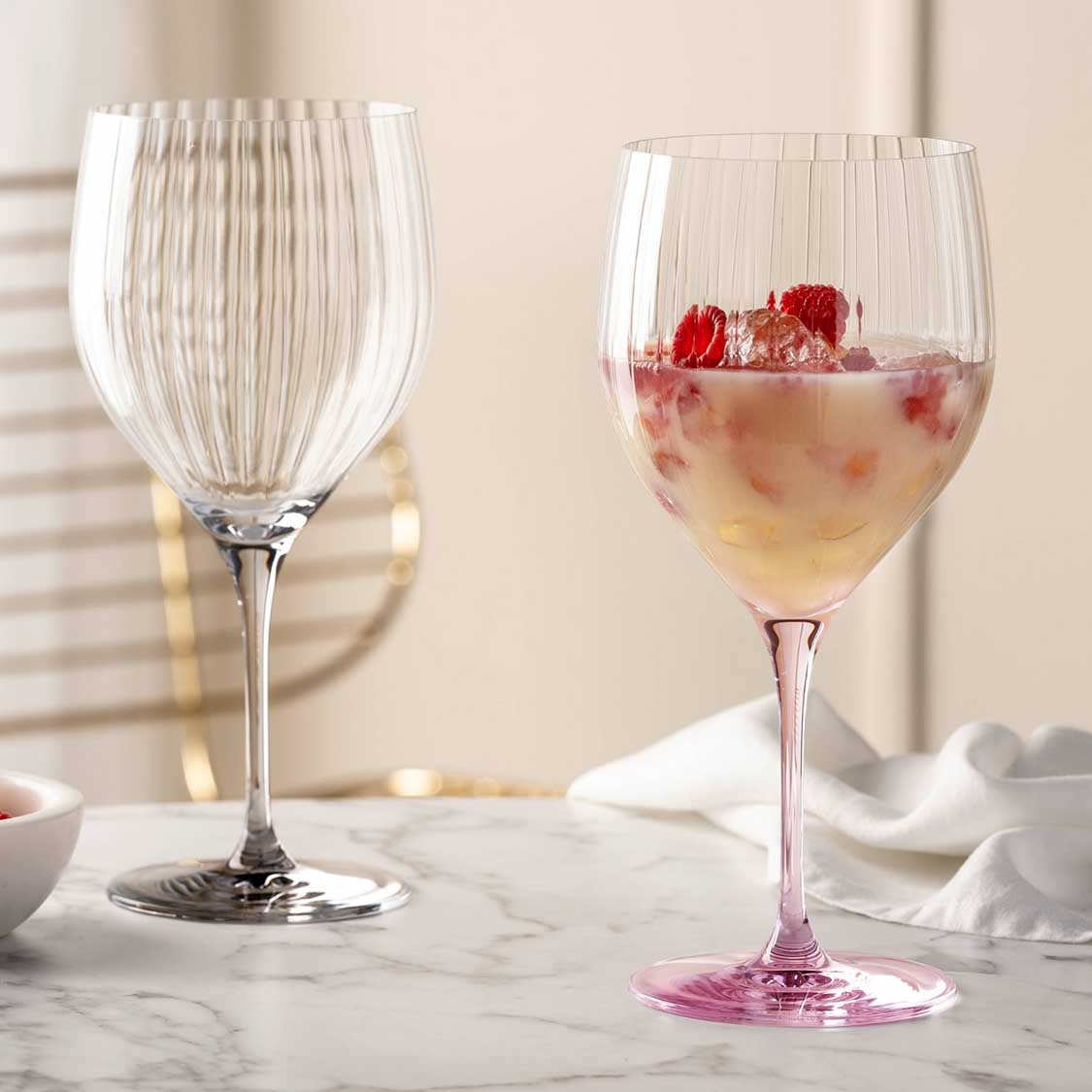 Cocktailglas POESIA rosé gefüllt mit Getränk und Himbeeren, daneben leeres Glas auf Marmortisch