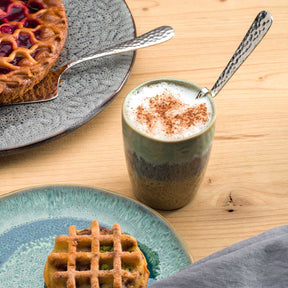 Keramikbecher MATERA mit Cappuccino auf Holztisch, daneben Waffel und Kuchen