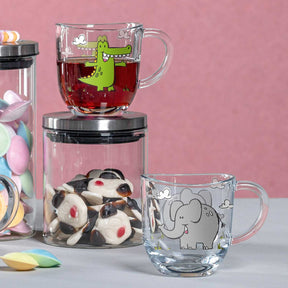 Tasse BAMBINI mit Elefantenmotiv neben Tasse mit Krokodilmotiv und Glasbehälter mit Süßigkeiten