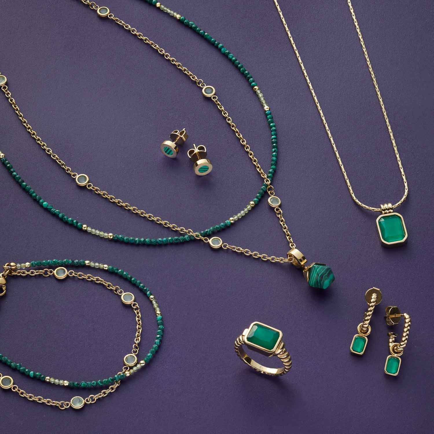 Grüner Schmuck aus Glas auf violettem Hintergrund, Halsketten, Ringe und Ohrringe in Grüntönen mit goldfarbenen Elementen