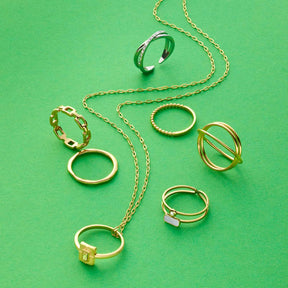 Goldene Ringe und Kette der Serie CIAO auf grünem Hintergrund arrangiert