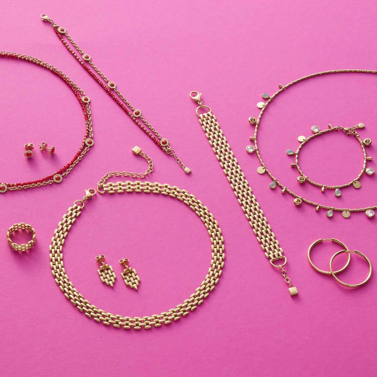 Goldener Schmuck-Set auf rosa Hintergrund, Ketten, Ringe und Ohrringe