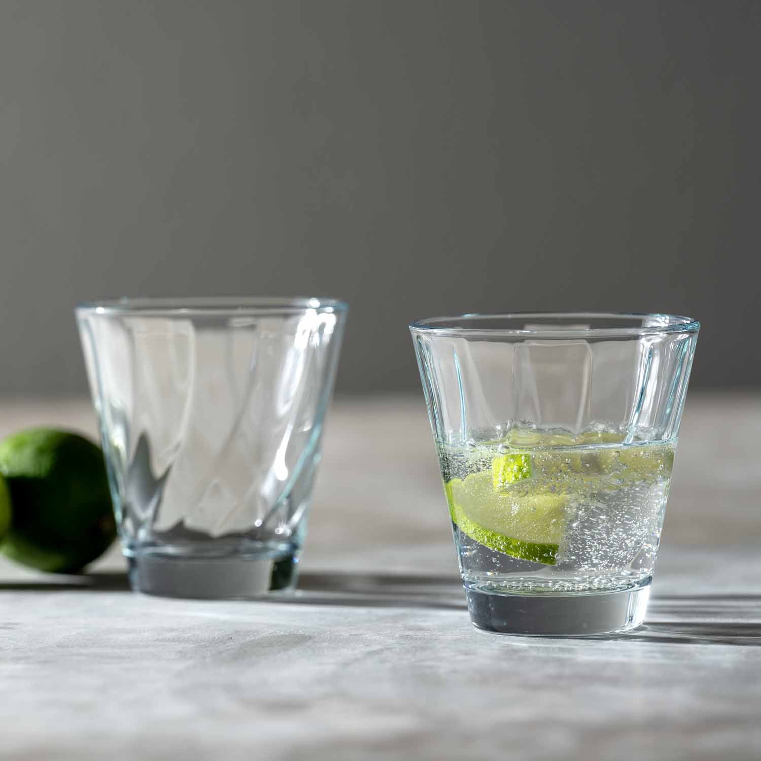 Trinkglas TWIST, eines leer, eines mit Limette und Wasser gefüllt, auf Marmortisch
