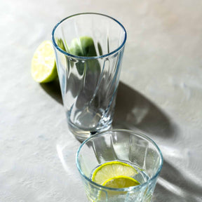 Trinkglas TWIST mit Limettenscheibe auf grauem Untergrund