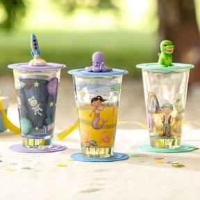 Drei Glasbecher mit farbigen Deckeln und Figuren im Freien auf Tisch