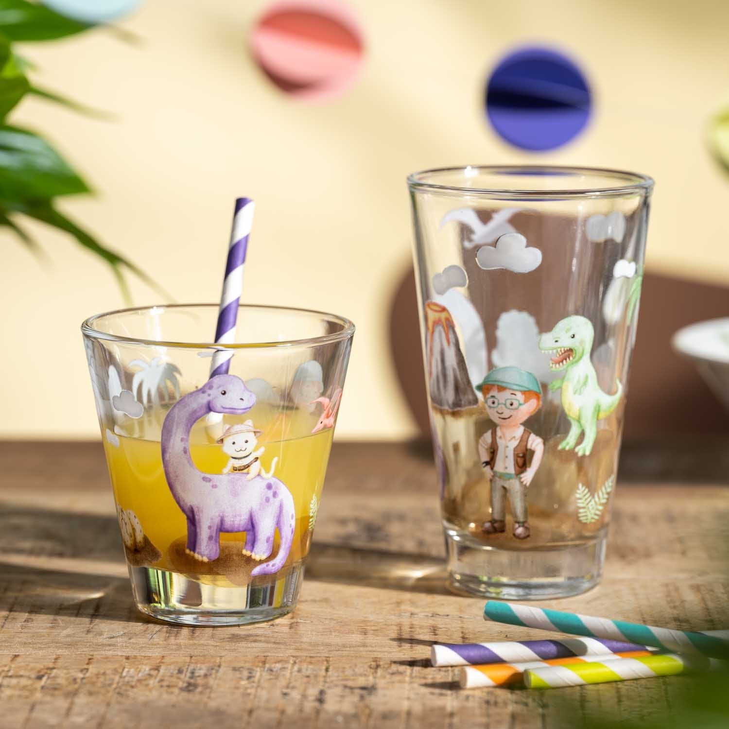 Trinkset BAMBINI AVVENTURA mit zwei Gläsern, Strohhalmen und Dinosaurier-Motiven auf Holztisch
