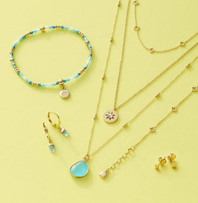 Schmuckkollektion mit Halsketten, Armband und Ohrringen aus Glas auf gelbem Hintergrund