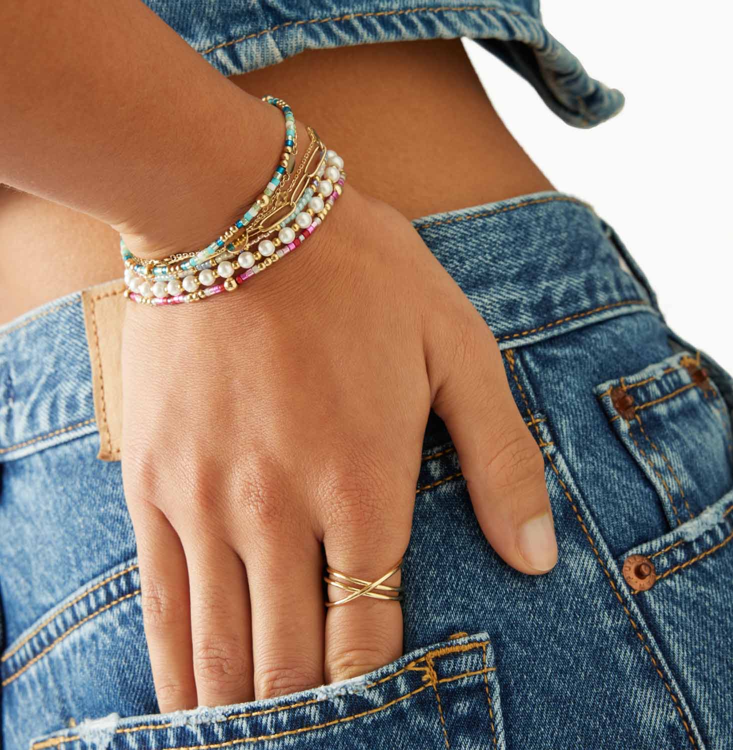 Frau trägt goldene Armbänder und Ring, Hand in Jeans-Tasche