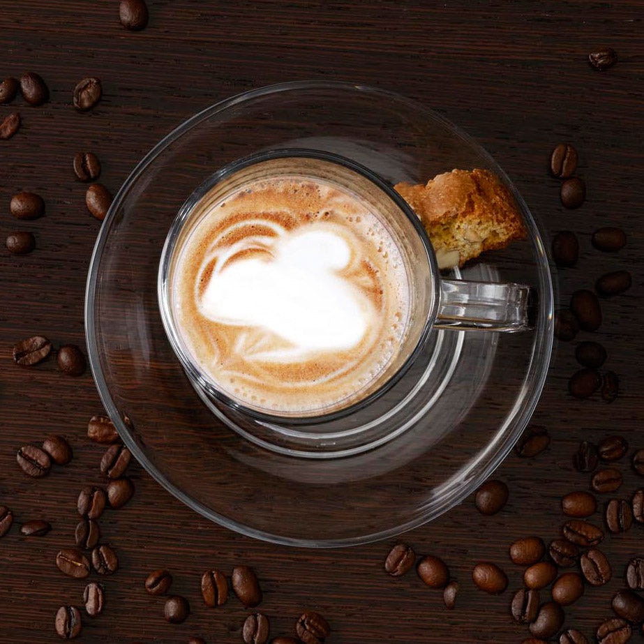 Glastasse SENSO mit Latte-Macchiato, umgeben von Kaffeebohnen und Gebäck