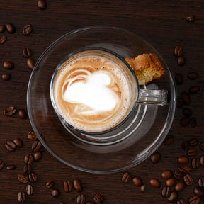 Glastasse SENSO mit Cappuccino und Latte-Art, umgeben von Kaffeebohnen