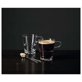 Glasbecher mit Kaffee, leerer Becher und Löffel auf schwarzer Oberfläche