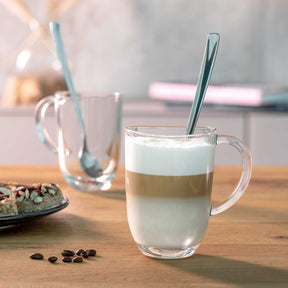 Zwei Latte Macchiato Tassen NAPOLI mit Löffeln auf Holztisch, eine gefüllt mit Getränk
