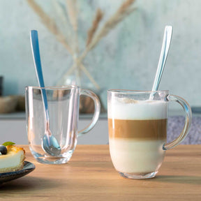 Zwei Latte Macchiato Tassen NAPOLI mit Löffeln auf Holztisch, eine gefüllt, eine leer