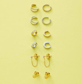 Verschiedene Ohrklemmen und Ohrringe in Silber und Gold auf gelbem Hintergrund