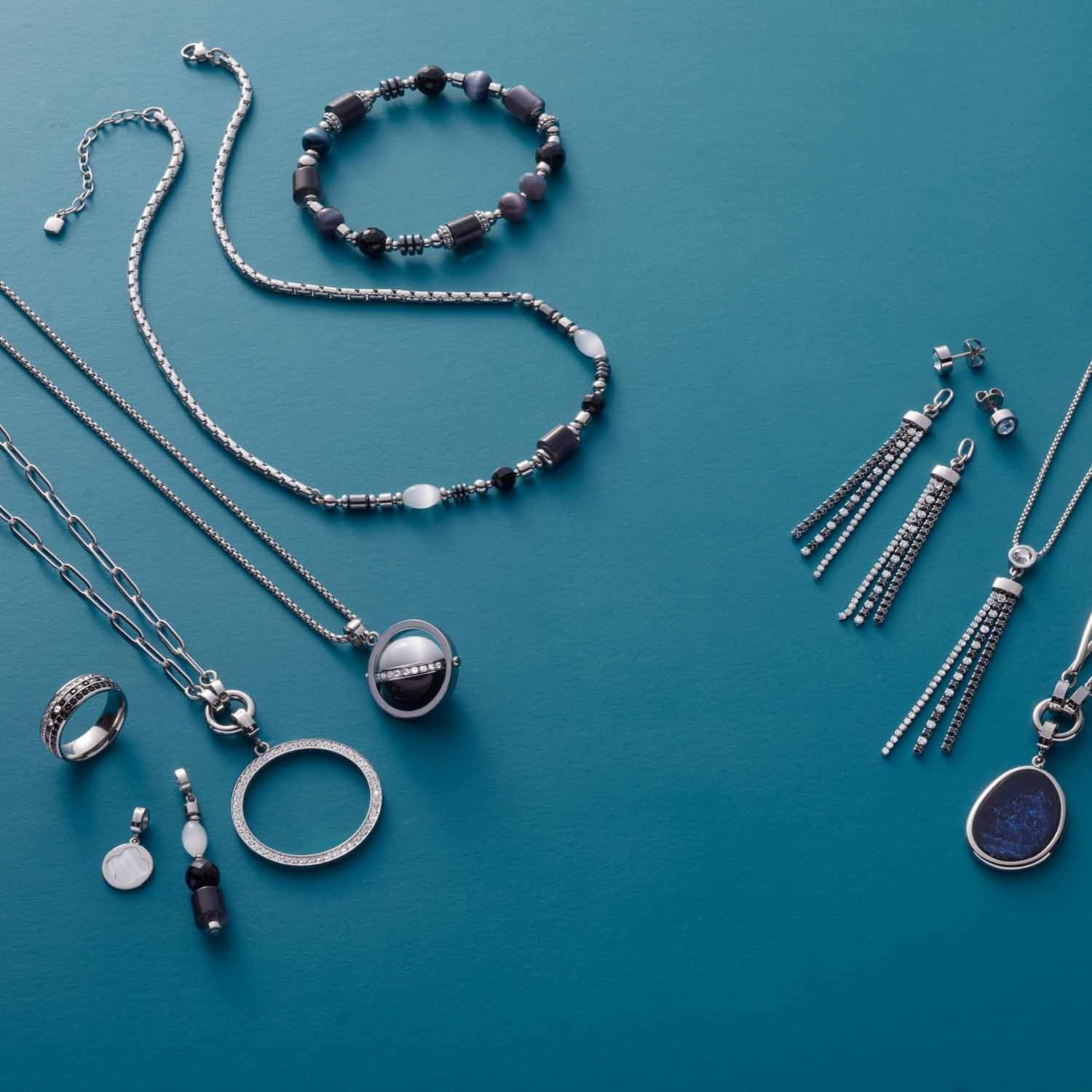 Schmuckkollektion mit Armband CASORIA silber und weiteren Schmuckstücken auf blauem Hintergrund