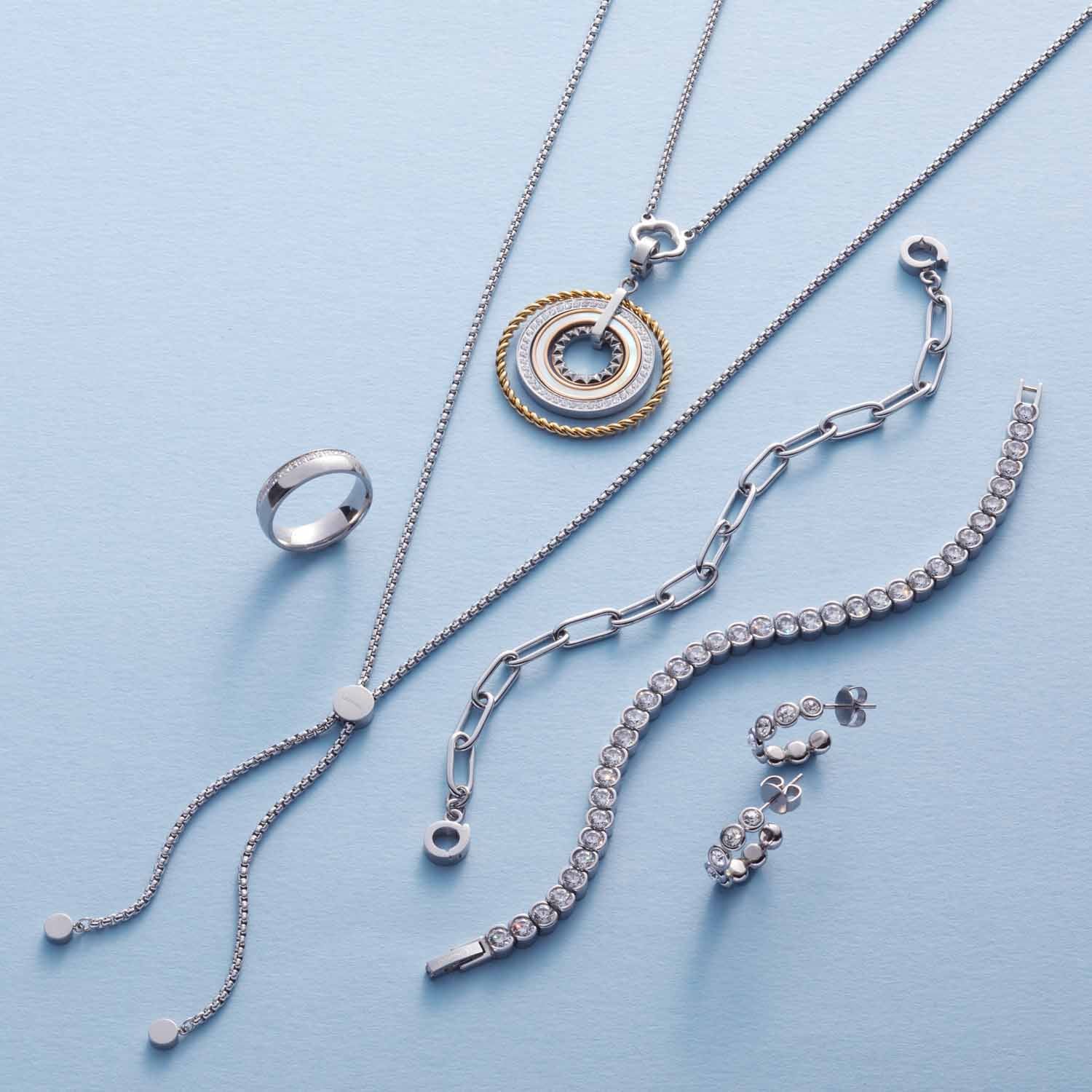 Silberne Schmuckstücke aus der Serie CREMONA auf hellblauem Hintergrund, darunter Armbänder, Ketten und Ringe