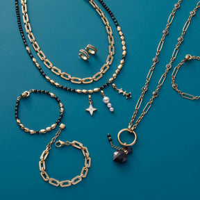Schmuckkollektion mit Armbändern, Ketten und Ohrringen in Gold und Schwarz auf türkisblauem Hintergrund