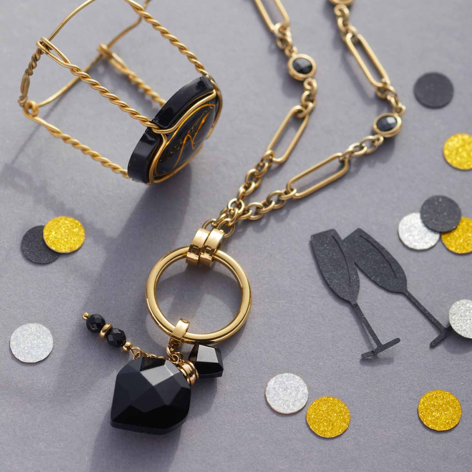 Halskette DELICA mit goldener Kette, schwarzem Herzanhänger und farbigen Glasperlen auf grauem Untergrund