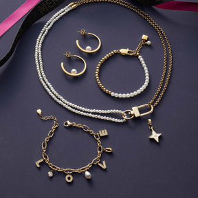 Schmuckkollektion mit goldenem Armband, Ohringen, Halskette und Perlenarmband auf grauem Untergrund
