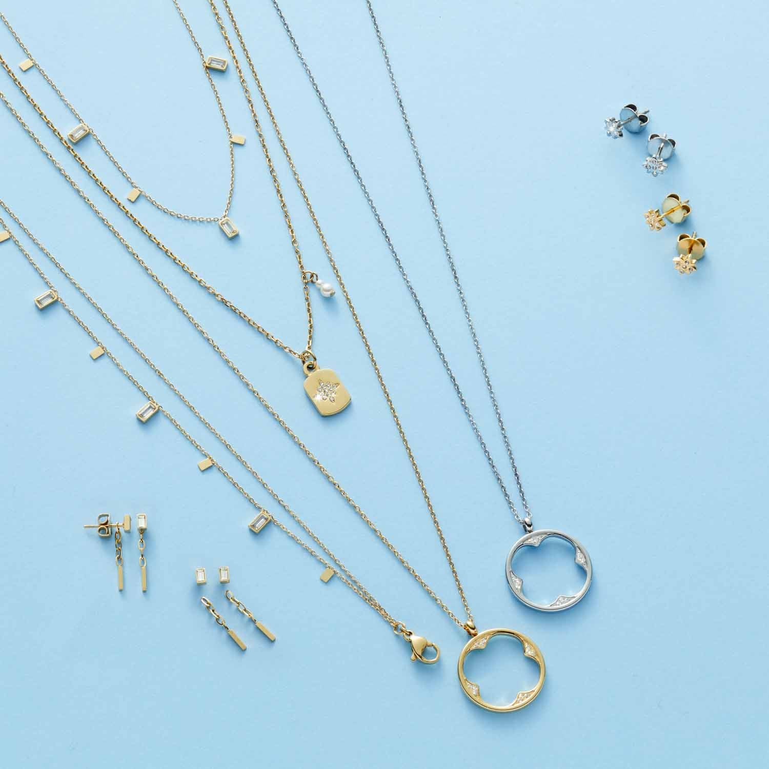 Schmuckkollektion mit Ohrsteckern, Halsketten und Ringen in Gold und Silber auf hellblauem Hintergrund