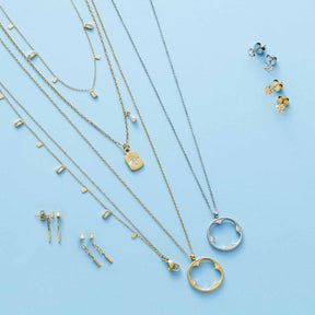 Schmuckkollektion mit Ohrsteckern, Halsketten und Ringen in Gold und Silber auf hellblauem Hintergrund