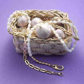 Halskette PATSY mit goldener Kette, Muscheln und Perlen auf violettem Hintergrund